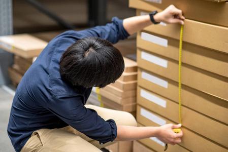 亚洲年轻人用卷尺测量纸板盒中产品尺寸.